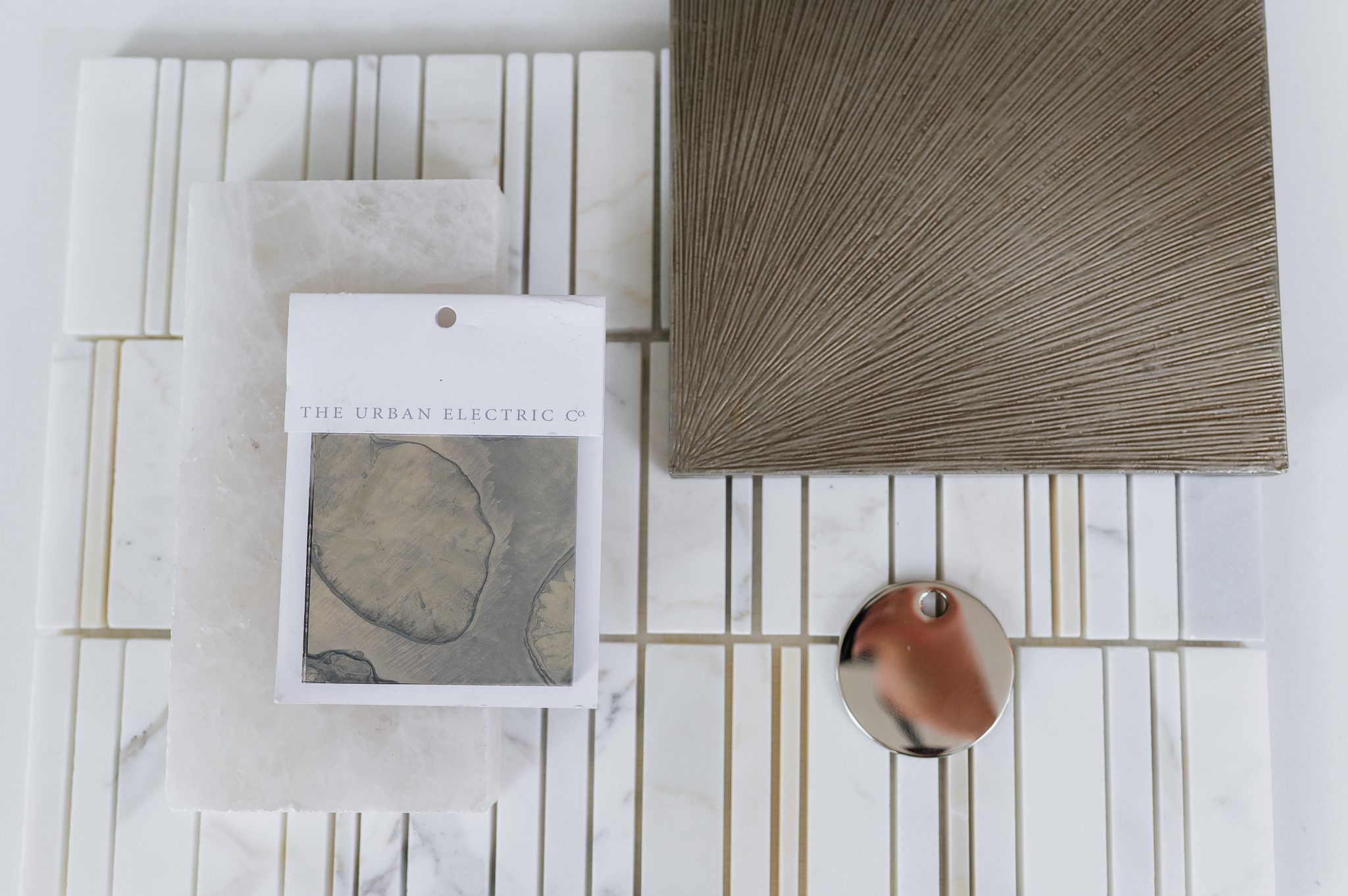 Interior design material samples with marble tile, textured panel, and polished hardware by LH Design Studio.
